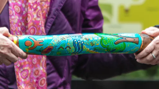 Painted aboriginal instrument being held at each end by a pair of hands