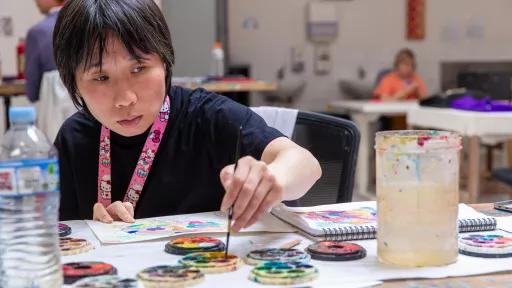 Artist Kittly Yui dipping a small paintbrush into a watercolour palette.