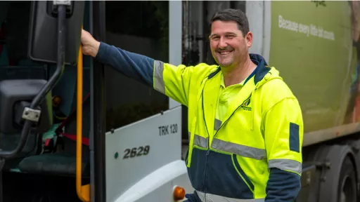 Waste truck driver in hi-vis shirt standing beside truck.