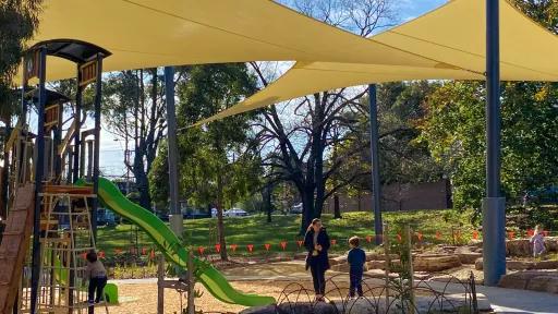 A woman and child stand beneath shade sails in a playground 