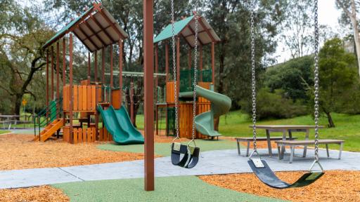 2 swings at a playground with climbing frames in the background