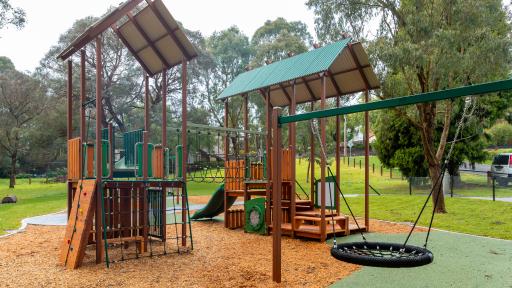 a basket swing and 2 covered slides and climbing frames at a playground