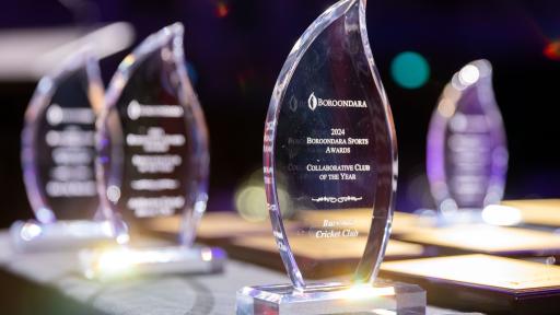 A close-up photograph of a collection of glass awards on a table. The central award is engraved with the text “BOROONDARA 2024 BOROONDARA SPORTS AWARDS COLLABORATIVE CLUB OF THE YEAR Burwood Cricket Club.” All the awards are flame-shaped.