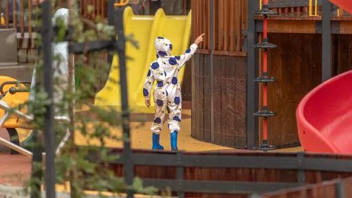 child in gumboots and raincoat pointing up at the playground