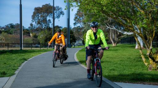 Two people on bikes riding directly towards the camera on a bike path. 