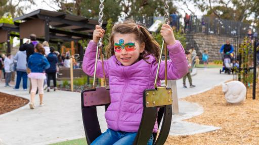 a child with colourful face paint is on the swings at a playground