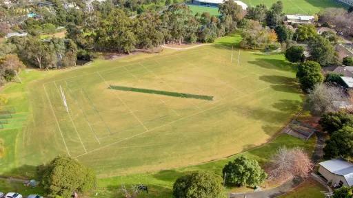 Aerial view of a large grassy sports oval surrounded by trees