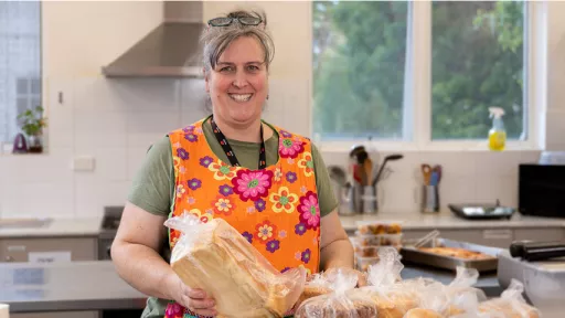 Woman wearing orange apron stands in kitchen holding bread 