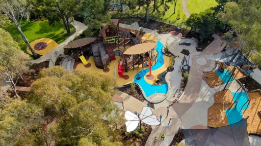 Drone image showing playground with timber play structures, play equipment and butterfly shade surrounded by parkland and trees