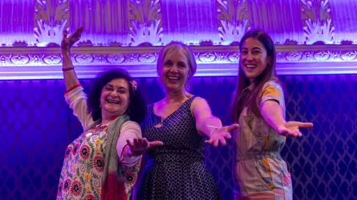 3 women throw their arms out on stage