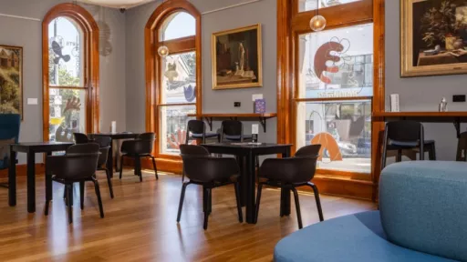 Room with timber floor, tall windows, paintings and tables and chairs