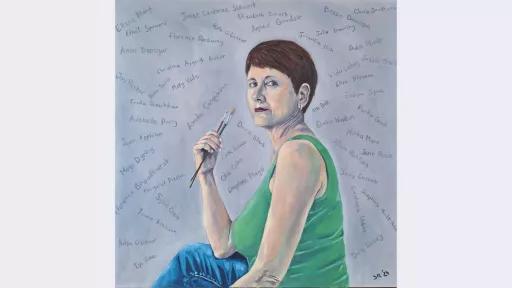 Portrait of a woman holding paintbrushes, set against a grey painted background with dozens of black handwritten names of women artists. She gazes confidently, wearing a green top and blue jeans, with the names suggesting a tribute or acknowledgment.