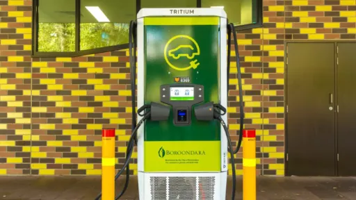 Green and white charger for electric vehicles in front of tiled wall.