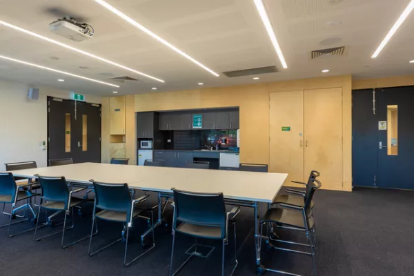 A room with a boardroom table and small kitchen behind it