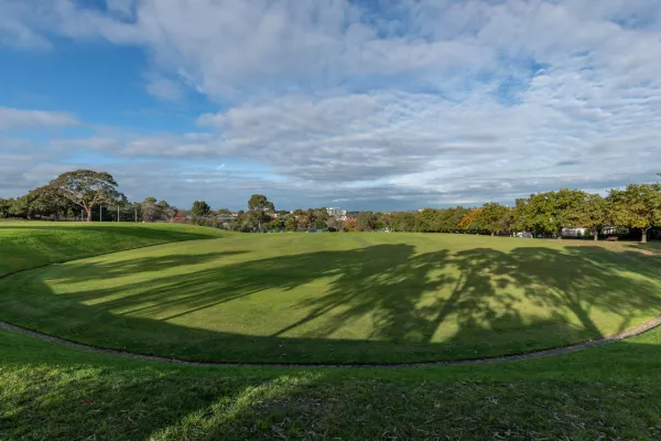 Oval-shaped grass field with a line of bricks around its boundary and sloped grass around its edge. 