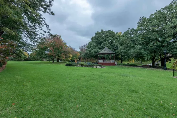 Large slightly sloped grass area with a small garden in the middle and trees around the edge. There is a rotunda and footpath on the far edge.