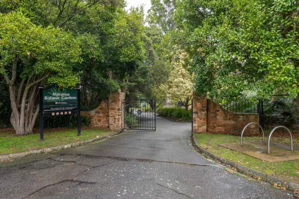 Steel entrance gate to Maranoa Botanic Gardens brick structures on either side. There is a sign on the left and a thick layer of trees.