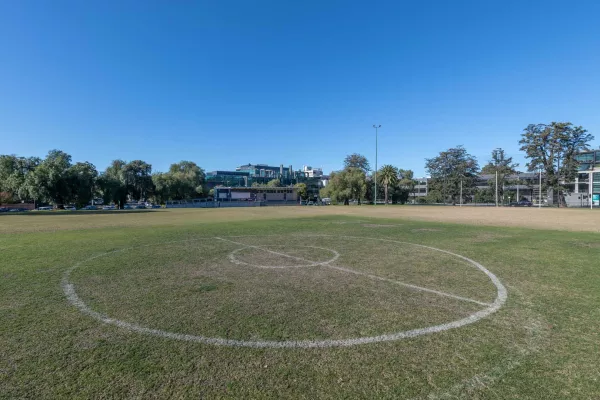 An open grass field with soccer line markings visible. In the background are residential houses and trees. 