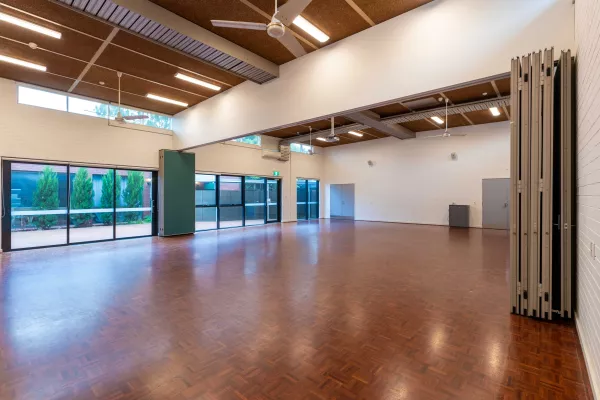 A large empty room with wooden floors and large windows looking into an outside courtyard