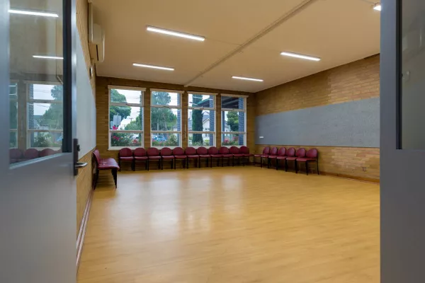 A small empty room with a wooden fall. Chairs lines the back wall of the room. Large windows look out towards the tress outside. 