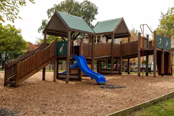 A wooden playground on a mulch surface. The playground ahs a slide and a ramp. 